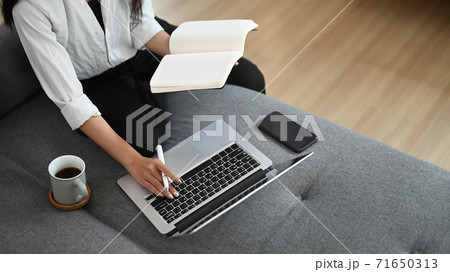 Cropped shot of a beautiful asian woman taking note and working with laptop on sofa at home. Cropped shot of a beautiful asian woman taking note and working with laptop on sofa at home. 71650313