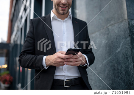 Elegant young man in a black suit holding a smartphone Elegant young man in a black suit holding a smartphone 71651992