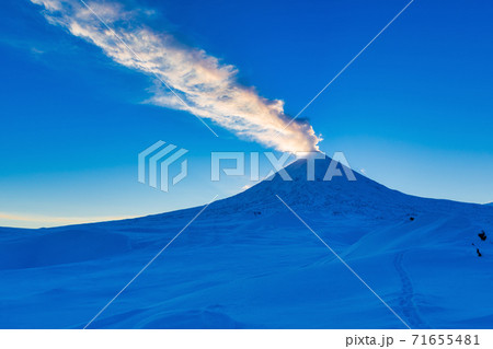 Kamchatka Peninsula, winter eruption active Volcano Klyuchevskaya Sopka at sunset, golden hour. Plume of ash, gas in blue sky 71655481