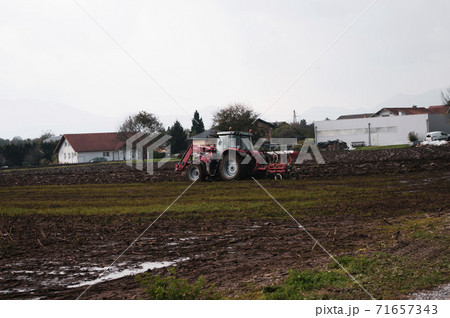 Red tractor plowing field in autumn season in the village 71657343