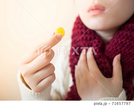 Female taking medical lozenges with honey lemon flavored for relief sore throat, irritating cough and mouth pain. Close up of girl with scarf feeling sick and cold in winter. Health care concept. Female taking medical lozenges with honey lemon flavored for relief sore throat, irritating cough and mouth pain. Close up of girl with scarf feeling sick and cold in winter. Health care concept. 71657797