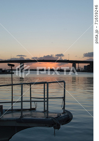 オレンジ色の夕焼けとシルエットの高架橋のある凪の港と船の先端 71659246