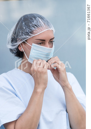 Portrait of a woman doctor putting on and fixing her surgical protective mask before her work shift Portrait of a woman doctor putting on and fixing her surgical protective mask before her work shift 71661367