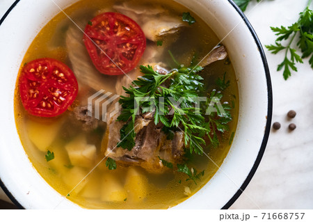 fish soup with carp, potatoes, parsley, tomato in enamel bowl stands on a board fish soup with carp, potatoes, parsley, tomato in enamel bowl stands on a board 71668757
