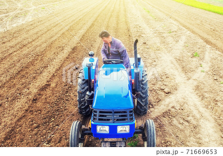 A farmer on a tractor cultivates a farm field. Soil milling, crumbling and mixing. Preparatory work for a new planting. Loosening surface, cultivating land for further planting. Agroindustry, farming. 71669653