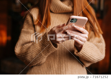 Close-up view of unrecognizable redhead woman wearing winter sweater typing message on mobile phone. Close-up view of unrecognizable redhead woman wearing winter sweater typing message on mobile phone. 71671252