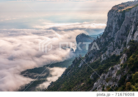 A majestic view of the rocky mountains and the valley in fog and clouds. Creamy fog covered the mountain valley in sunset light. Picturesque and gorgeous scene. Misty sunset over Crimea Mountains 71676008