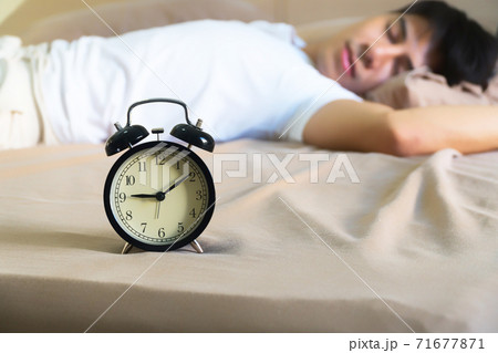 black alarm clock with handsome man sleeping on the bed. He was tired from work until late. 71677871