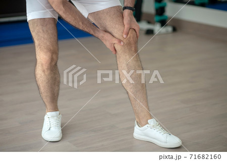 Close-up of male hands massaging painful knee in the gym Close-up of male hands massaging painful knee in the gym 71682160