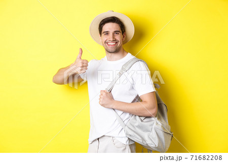 Tourism, travelling and holidays concept. Happy man going on vacation, holding backpack and showing thumb up, smiling satisfied, standing against yellow background Tourism, travelling and holidays concept. Happy man going on vacation, holding backpack and showing thumb up, smiling satisfied, standing against yellow background 71682208