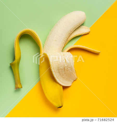 Half peeled banana on green and yellow background Half peeled banana on green and yellow background 71682524