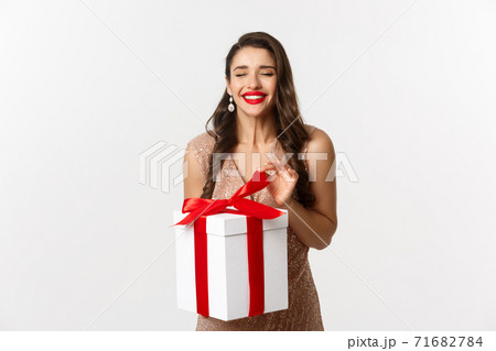 Merry Christmas. Charming woman in elegant dress open gift box and smiling delighted, unwrapping a present, standing over white background Merry Christmas. Charming woman in elegant dress open gift box and smiling delighted, unwrapping a present, standing over white background 71682784