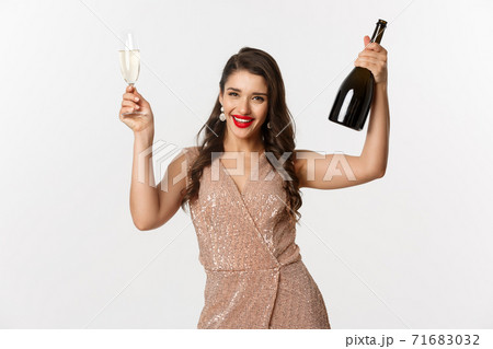 Winter holidays celebration concept. Excited beautiful woman in dress raising glass of champagne for toast, enjoying Christmas party, standig over white background Winter holidays celebration concept. Excited beautiful woman in dress raising glass of champagne for toast, enjoying Christmas party, standig over white background 71683032