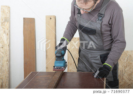 Carpenter working with  electric sheet finishing sander  on wood lath on desk, on background oriented strand board 71690377