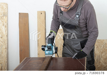 Carpenter working with  electric planer on wood lath on desk, on background oriented strand board 71690378