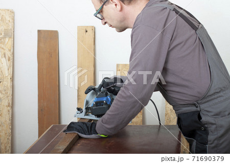 Carpenter cuts wood lath electric hand tool circular saw on desk, on background oriented strand board Carpenter cuts wood lath electric hand tool circular saw on desk, on background oriented strand board 71690379