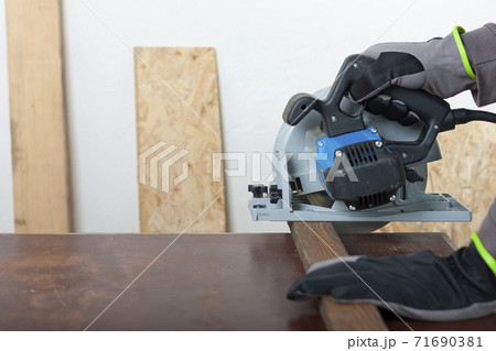 Carpenter cuts wood lath electric hand tool circular saw on desk, on background oriented strand board 71690381