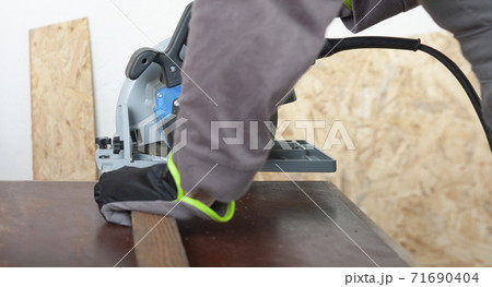 Carpenter cuts wood lath electric hand tool circular saw on desk, on background oriented strand board Carpenter cuts wood lath electric hand tool circular saw on desk, on background oriented strand board 71690404
