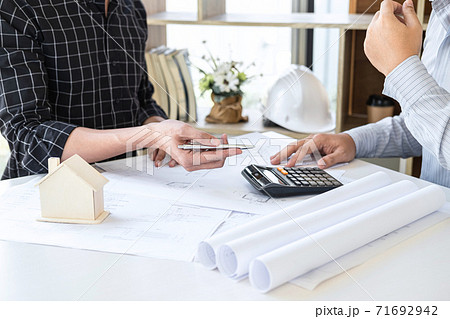 Construction engineering or architect discussing a blueprint and building model while checking information on sketching meeting for architectural project in work site 71692942