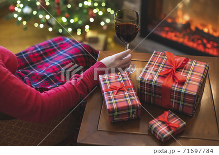Alone woman covered plaid with glass of wine sitting and relaxation on armchair near fareplace and christmas tree after finishing pakking gift boxes for family. Alone woman covered plaid with glass of wine sitting and relaxation on armchair near fareplace and christmas tree after finishing pakking gift boxes for family. 71697784