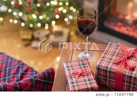 Armchair with plaid, packing gift boxes for family and glass of wine near christmas tree and fireplace. Top view 71697786