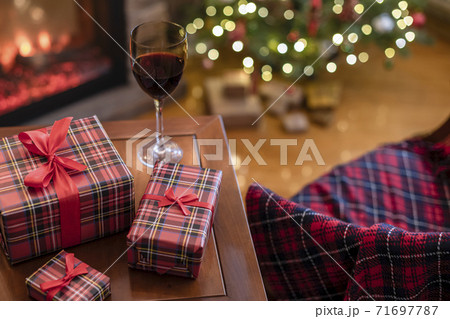 Armchair with plaid, packing gift boxes for family and glass of wine near christmas tree and fireplace. Top view Armchair with plaid, packing gift boxes for family and glass of wine near christmas tree and fireplace. Top view 71697787