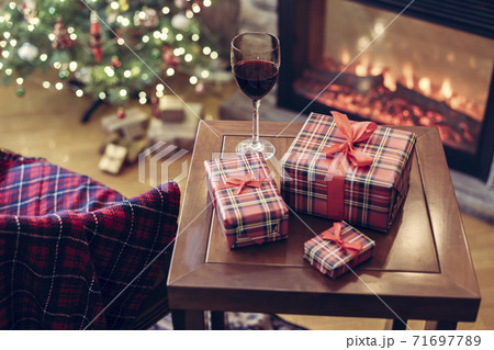 Armchair with plaid, packing gift boxes for family and glass of wine near christmas tree and fireplace. Top view Armchair with plaid, packing gift boxes for family and glass of wine near christmas tree and fireplace. Top view 71697789
