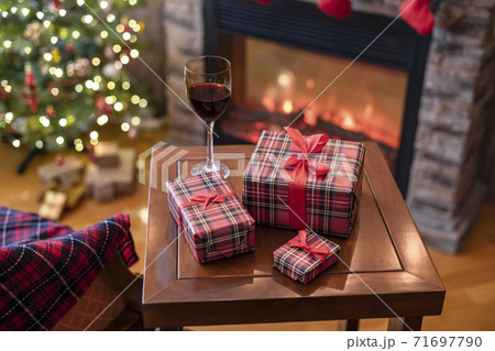 Armchair with plaid, packing gift boxes for family and glass of wine near christmas tree and fireplace. Top view Armchair with plaid, packing gift boxes for family and glass of wine near christmas tree and fireplace. Top view 71697790
