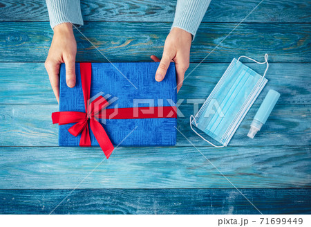 Woman's hands holding present box. Conceptual symbol of the Christmas in pandemia of COVID19. 71699449