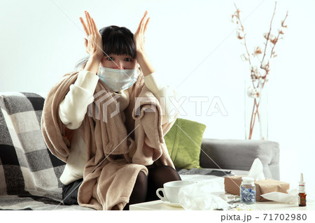 Woman wrapped in a plaid and wearing face mask trying to protect herself from somebody's sick near by 71702980