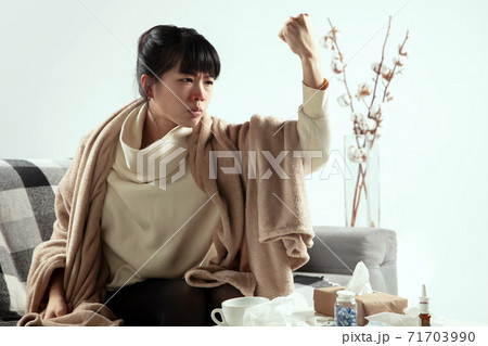 Woman wrapped in a plaid looks sick, ill, sneezing and coughing sitting at home indoors Woman wrapped in a plaid looks sick, ill, sneezing and coughing sitting at home indoors 71703990