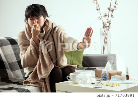 Woman wrapped in a plaid looks sick, ill, sneezing and coughing sitting at home indoors 71703991