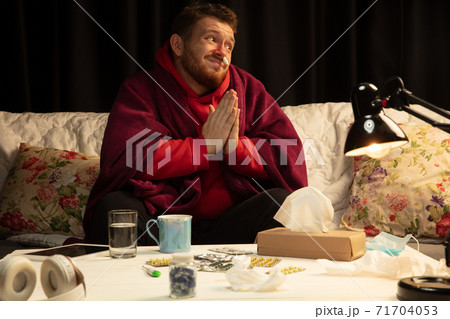 Man wrapped in a plaid looks sick, ill, sneezing and coughing sitting at home indoors 71704053