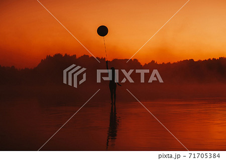 surreal silhouette of a girl with a balloon in her hand on the water surreal silhouette of a girl with a balloon in her hand on the water 71705384