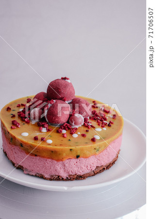 Raw vegan raspberry cake decorated with berry truffles. Mango filling jelly vegetarian cashew cream cheesecake gluten free. Lactose sugar free desert on white plate. Indoor photo Raw vegan raspberry cake decorated with berry truffles. Mango filling jelly vegetarian cashew cream cheesecake gluten free. Lactose sugar free desert on white plate. Indoor photo 71706507