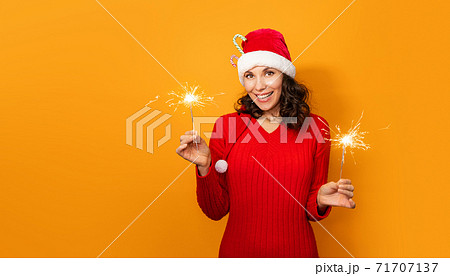 Young happy woman with sparklers celebrate and laugh on orange background. New Year and Christmas celebration concept. Young girl in santa claus hat on bright color background, copy space 71707137