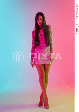 Beautiful seductive girl in fashionable dress, outfit on bright gradient pink-blue background in neon light 71709542
