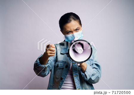 Asian woman wearing protective face mask shouting with megaphone isolated over white background. Asian woman wearing protective face mask shouting with megaphone isolated over white background. 71720500