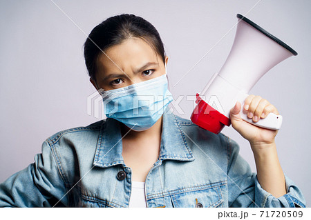 Asian woman wearing protective face mask shouting with megaphone isolated over white background. Asian woman wearing protective face mask shouting with megaphone isolated over white background. 71720509