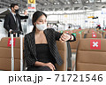 Young businesswoman wearing face mask sitting at the airport and looking on her watch to check time to on board. 71721546