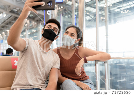 Young couple man and woman wearing face mask selfie by smartphone while waiting to on board in the airport. Young couple man and woman wearing face mask selfie by smartphone while waiting to on board in the airport. 71725650