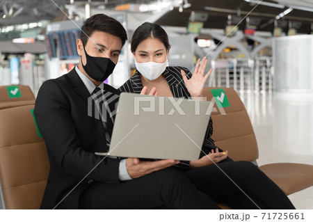 Businesswoman wearing face mask having gesture hand at laptop to say good bye with colleague at the other side of video conference after online meeting finished. 71725661