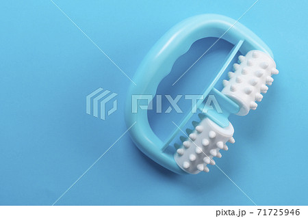 Anti-cellulite manual turquoise plastic massager with silicone rollers with pimples on a blue bright background. The use of an individual tool to enhance skin health and improve blood circulation 71725946