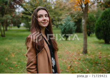 Portrait of young attractive woman in park. Woman in beige coat 71729421