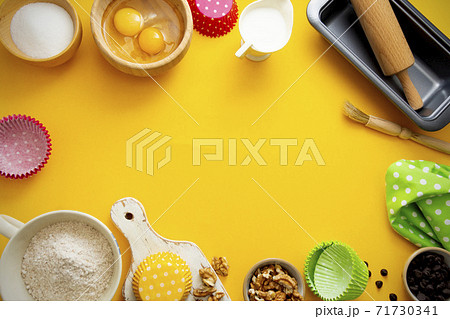 Baking frame with flour, sugar, milk, eggs, wallnuts, chocolate chips, rolling pin, baking mold. Yellow background with copy space. Baking frame with flour, sugar, milk, eggs, wallnuts, chocolate chips, rolling pin, baking mold. Yellow background with copy space. 71730341