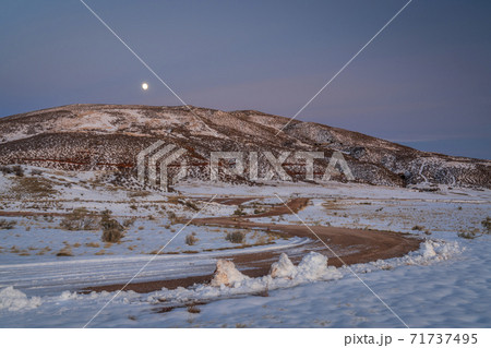 windy country road covered by snow in mountain valley 71737495