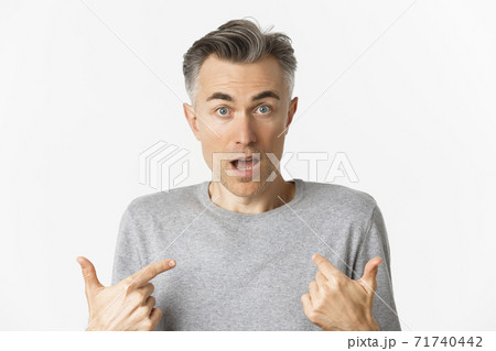 Close-up of confused middle-aged man, pointing at himself and gasping, standing over white background Close-up of confused middle-aged man, pointing at himself and gasping, standing over white background 71740442