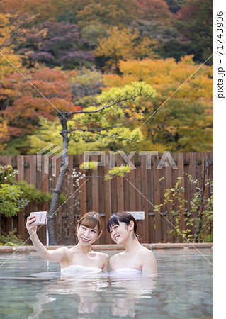 紅葉バックに露天風呂で撮影をする若い女性2人組 紅葉バックに露天風呂で撮影をする若い女性2人組 71743906