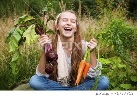 European girl 11 years old sitting on the grass, holding fresh carrots and beets and laughing European girl 11 years old sitting on the grass, holding fresh carrots and beets and laughing 71757715