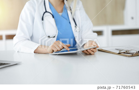 Unknown woman-doctor sitting in sunny clinic and using tablet pc, close-up. Data and best service in medicine Unknown woman-doctor sitting in sunny clinic and using tablet pc, close-up. Data and best service in medicine 71760543